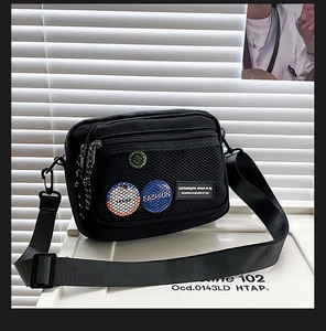 Detail of black canvas crossbody bag featuring colorful decorative badges on front mesh pocket