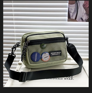 Detail of green canvas crossbody bag featuring a mesh pocket and decorative badges