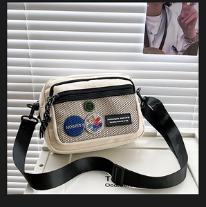 Detail of off-white canvas crossbody bag with mesh pocket and decorative badges
