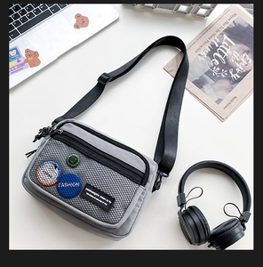 Detail of grey canvas crossbody bag with mesh pocket and trendy patches on a desktop