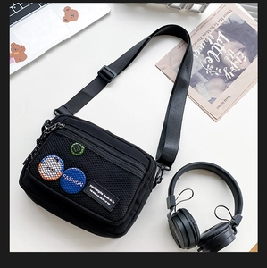 Detail of black canvas crossbody bag with mesh pocket and trendy badge decorations