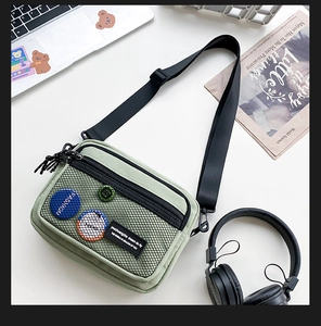Flat lay of olive green canvas crossbody bag with mesh pocket on a modern desk setup