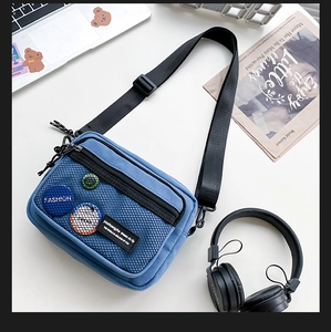 Close-up of blue canvas messenger bag with black mesh pocket and decorative badges