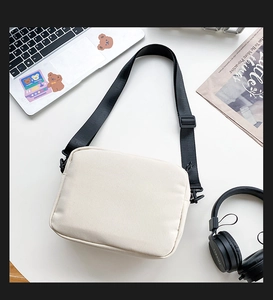 Minimalist cream canvas messenger bag with adjustable strap on a workspace desk