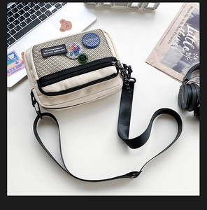 Detailed view of cream canvas crossbody bag with black mesh pocket and colorful cartoon pins