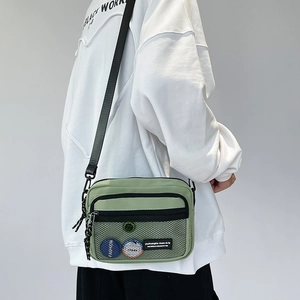 Detail view of a green nylon messenger bag with front mesh pocket and fashion badge