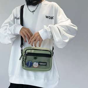 Detail of light green canvas crossbody bag featuring mesh pocket and fashion badges
