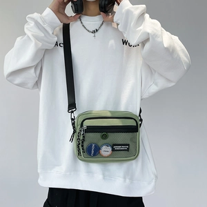 Detail of light green canvas crossbody bag featuring front mesh pocket and fashion badges