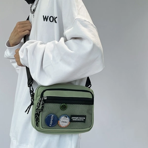 Detail of light green canvas messenger bag featuring a mesh pocket and fashion badges