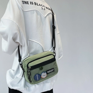 Detail of light green canvas crossbody bag with black mesh pocket and decorative badges