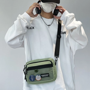 Detail of light green canvas crossbody bag with mesh pocket and stylish badges