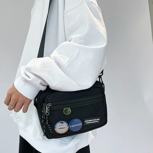 Detail view of black canvas crossbody bag featuring a front mesh pocket and stylish badges