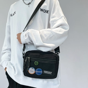 Detailed view of black nylon crossbody bag with mesh pocket and decorative badges