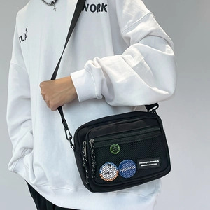 Detail of black canvas crossbody bag featuring a front mesh pocket and colorful badges