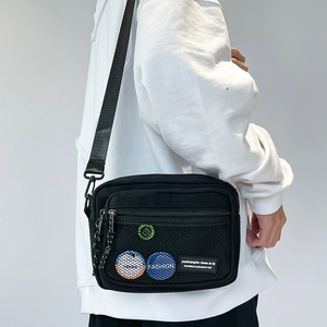 Detail view of black canvas messenger bag featuring a mesh pocket and colorful badges