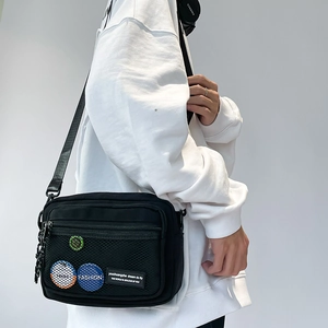 Detail view of black canvas crossbody bag featuring mesh pocket and fashion patches