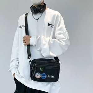 Detail of black canvas crossbody bag featuring mesh pocket and fashion badge on model