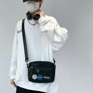 Detail of black canvas messenger bag with mesh pocket and colorful fashion badges