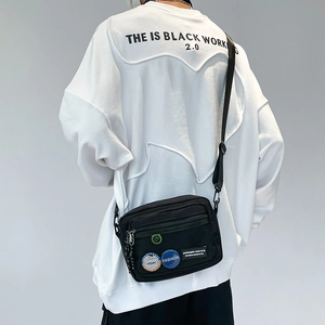 Close-up of black canvas crossbody bag featuring mesh pocket and colorful badges