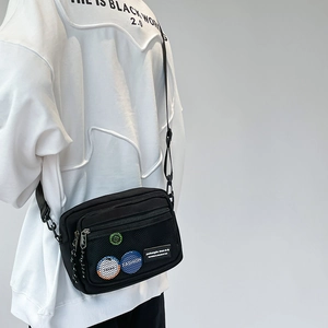Detail view of black canvas crossbody bag with mesh pockets and colorful fashion patches