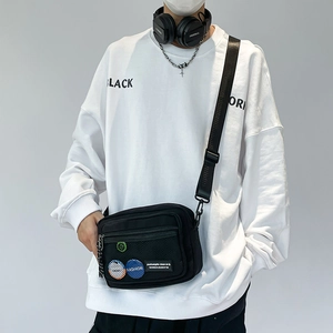 Detail of a black canvas crossbody bag featuring a front mesh pocket and colorful badges