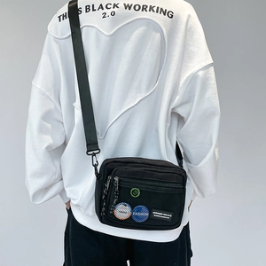 Macro shot of black canvas crossbody bag featuring mesh pocket and colorful badges on the front