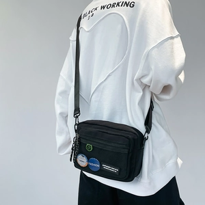 Close-up of black streetwear messenger bag with functional pockets and stylish badges