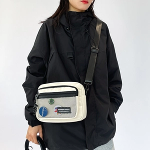 Close-up of minimalist cream canvas crossbody bag with mesh pocket and fashion slogan details
