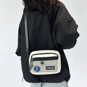 Detail showing white canvas crossbody bag with black mesh front pocket and badges