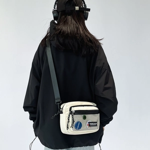 Close-up of a white canvas crossbody bag with mesh pocket and black nylon shoulder strap