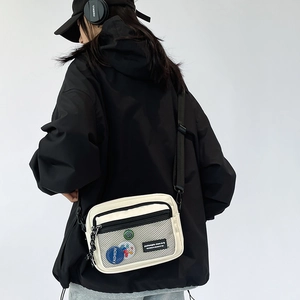 Detailed view of white canvas crossbody bag featuring a black mesh pocket and badge detail