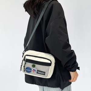 Detail of canvas shoulder bag with black mesh pocket and fashion badge on the side