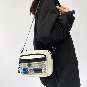 Close-up of white canvas crossbody bag featuring black mesh pocket and trendy badges