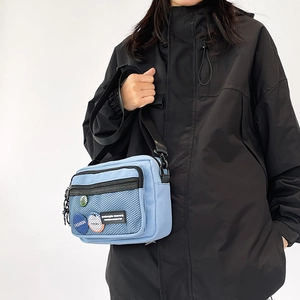 Detail of light blue canvas crossbody bag featuring black mesh pocket and decorative badges