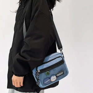 Detail of light blue canvas crossbody bag with mesh pocket and decorative badges