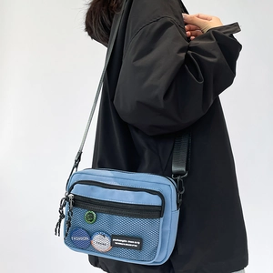 Close-up of light blue canvas crossbody bag with mesh pocket and trendy fashion badges