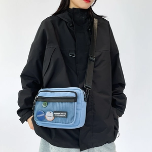 Close-up of light blue nylon crossbody bag with black mesh pocket and trendy fashion labels