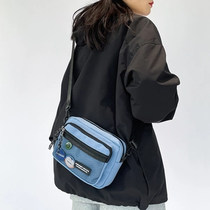 Detailed back view of a light blue canvas crossbody bag with mesh pocket and badges