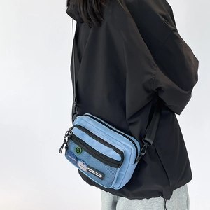 Detail of light blue casual canvas crossbody bag with black mesh pocket and strap