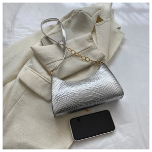 Detail of silver faux snake skin shoulder bag with gold chain strap on white blazer