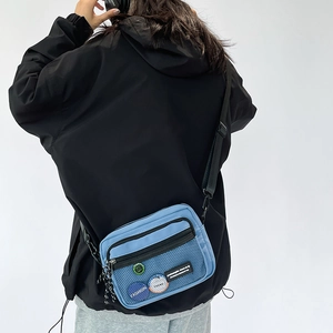 Rear view of a model wearing a small light blue nylon crossbody bag with mesh pocket detail