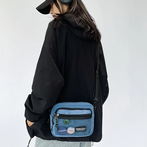 Blue crossbody bag with black mesh pocket and badges shown on a model in a hoodie