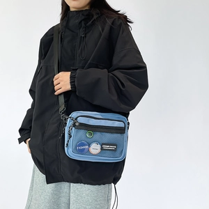 Detail view of light blue nylon crossbody bag with mesh pocket and colorful badges