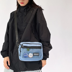Detail of light blue canvas crossbody bag showing mesh pocket and brand patches