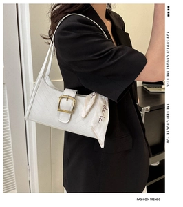 Detail of white leather baguette bag with gold buckle and decorative silk scarf accessory