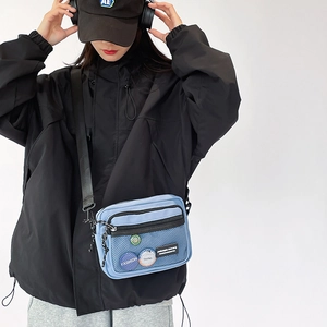Detail of light blue canvas crossbody bag featuring front mesh pocket and colorful badges