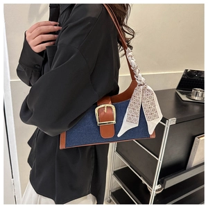 Détail d'un sac à bandoulière en denim bleu avec bordure en cuir marron et foulard décoratif