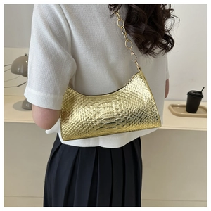 Detail of a shiny gold crocodile-patterned shoulder bag with thick round chain strap