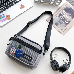 Detailed view of grey canvas crossbody bag with mesh pocket and trendy badges on flat lay desk