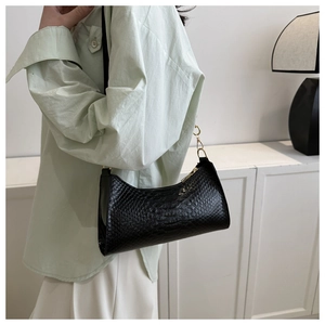 Detail of glossy black crocodile-pattern faux leather underarm bag with gold metal hardware